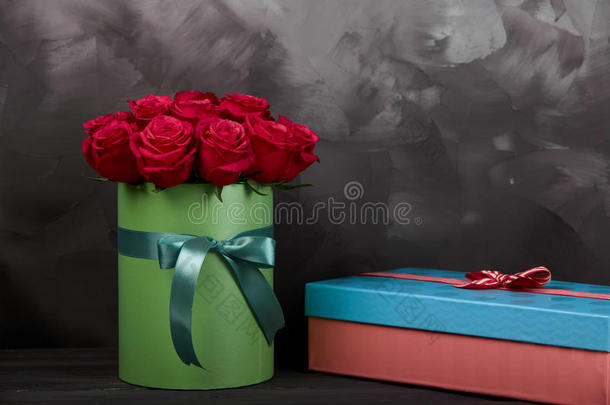 一束精致的红色玫瑰，绿色礼品盒，深灰色的乡村木制背景。 家居装饰。