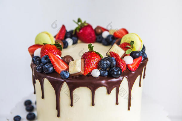 美丽的奶油色蛋糕装饰草莓，蓝莓，巧克力，马卡龙，站在白色的木桌上