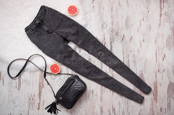 灰色高腰牛仔裤，黑色手提包和切西柚半部。 木制背景。 时尚概念。