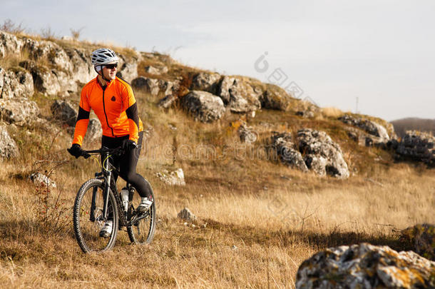 骑着橙色夹克的自行车在岩石小径上骑自行车。 极限运动概念。 文本的空间。