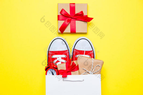 大红色胶鞋，美丽的礼物和闹钟在凉爽的购物袋上美妙的黄色背景