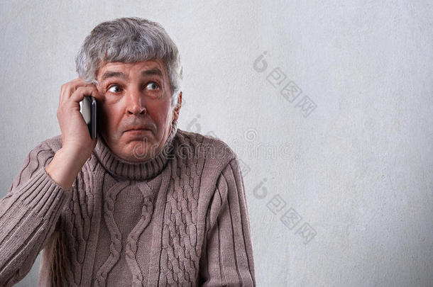 一个退休的人在谈论智能手机，<strong>惊讶</strong>地接到电话。 穿着毛衣的成熟男人的<strong>惊讶表情</strong>