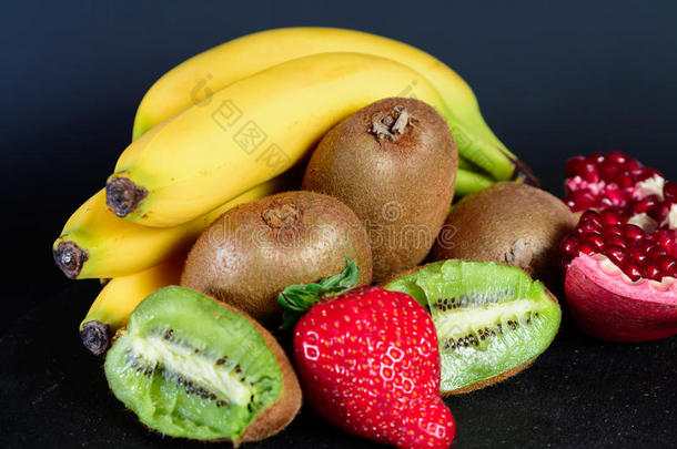 新鲜有机猕猴桃、草莓、香蕉和半石榴石在黑色圆形、新鲜水果、早上好食物上的位置。