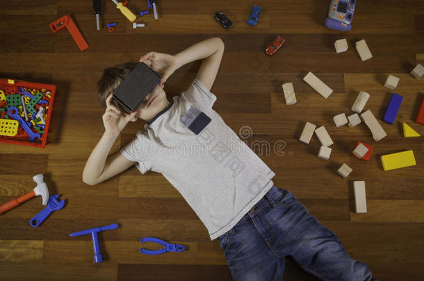 儿童与三维虚拟现实，虚拟现实纸板眼镜躺在木地板上。他身边有很多玩具