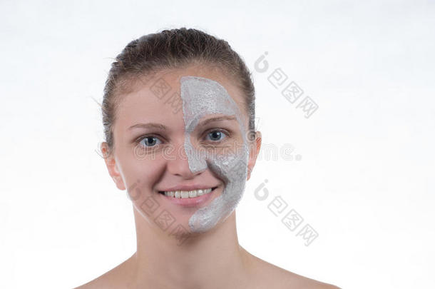 灰色粘土的化妆品面具，白色背景上的一个年轻女孩的脸上有磨砂