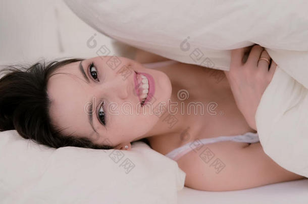 新鲜快乐的黑发女人在家里睡觉。 美丽的女孩躲在毯子下面微笑。