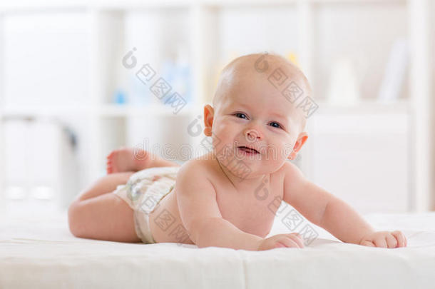 婴儿男孩穿着尿布躺在床上，在白光卧室或托儿所。 儿童纺织品和床上用品。