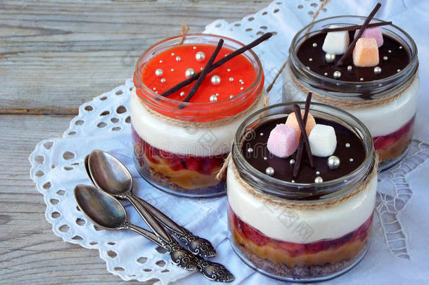 木制背景的玻璃瓶中的奶酪蛋糕甜点。 巧克力饼干，咸焦糖，草莓果冻，奶酪慕斯，巧克力