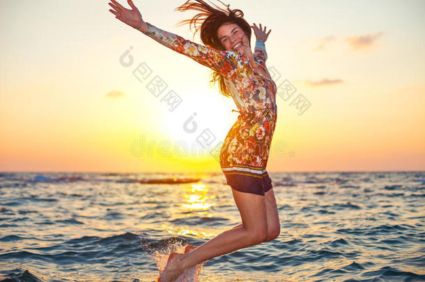 美丽的女孩穿着五颜六色的衣服，在日落时跳入海水中