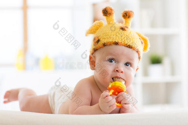 戴着长颈鹿帽子的有趣的小男孩躺在托儿所的肚子上。 小孩子用咬人玩具。