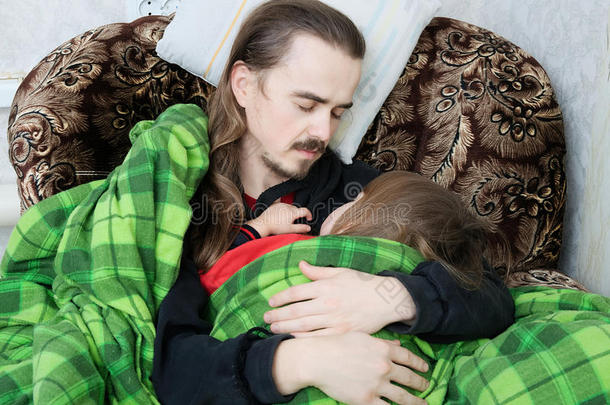 父亲和孩子睡在扶手椅上。 家人休息。 幸福的父母，父爱。 爸爸和女儿裹着毯子