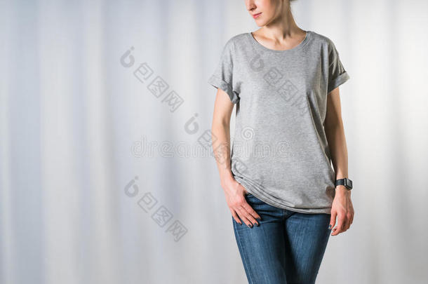 站在浅灰色背景上的年轻女子，穿着浅灰色T恤和蓝色牛仔裤
