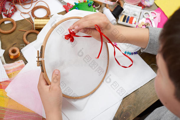 男孩刺绣在箍，手特写和红色丝带在白色纺织品，学习缝纫，工作培训，手工和手工艺公司