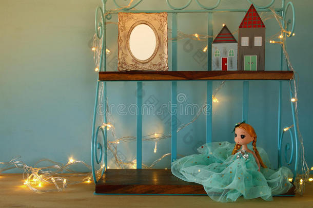 可爱的娃娃，空白的相框和木制的小房子旁边温暖的花环灯