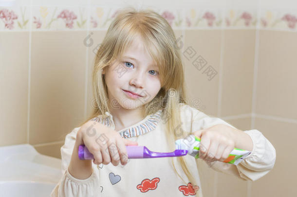 漂亮的女孩在电动牙刷上得到牙膏。