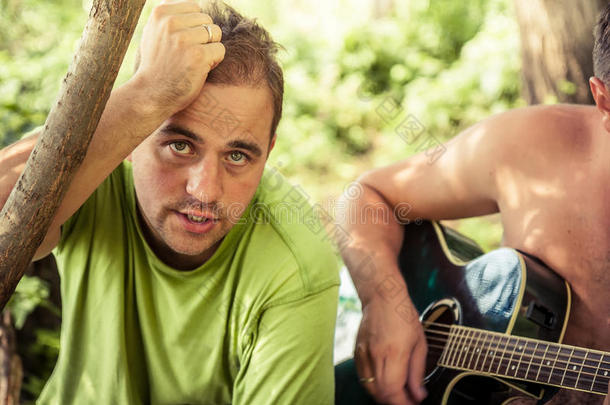 在户外野营派对上，一个真诚的年轻人在树叶间用吉他唱歌