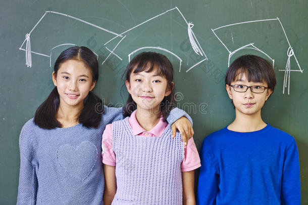 亚洲小学生站在粉笔画的博士帽下面