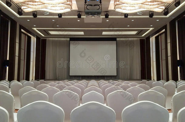 会议室有天花板LED灯，一排白色椅子，有舞台和空屏幕，用于商务会议、会议