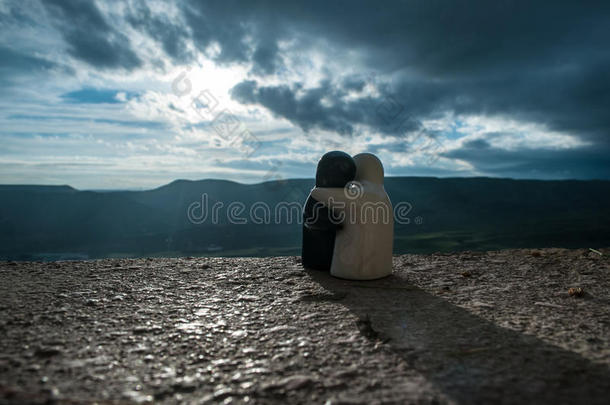 一对陶瓷人物拥抱在背景山日落，剪影两个浪漫的人拥抱和看后景