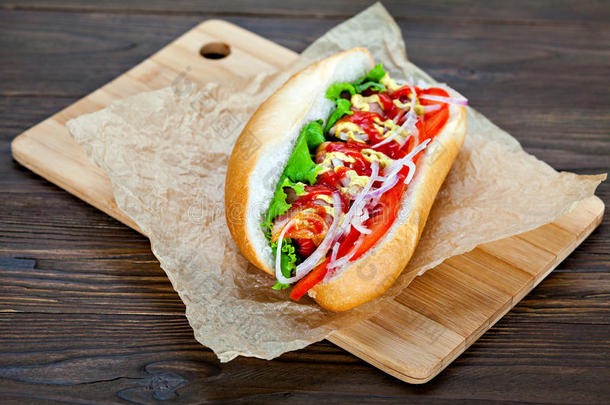 大美味的热狗，酱汁和蔬菜在羊皮纸上的木制背景。 热狗美食家