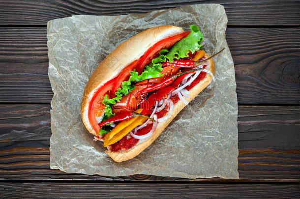 大美味的热狗，酱汁和蔬菜在羊皮纸上的木制背景。 热狗美食家。