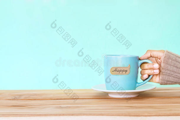 手拿一个咖啡杯杯子，在木<strong>桌</strong>上贴上快乐的单词标<strong>签</strong>，浪漫和爱情背景。 快乐和放松的概念