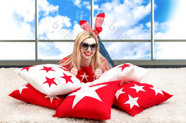 戴眼镜的漂亮的年轻金发女人躺在枕头上。 漂亮的枕头来装饰房子的内部。 带枕头的