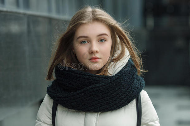 城市肖像年轻美丽的金发时尚女孩在春季秋季户外摆姿势，白色外套，黑色针织围巾。 古董鱼