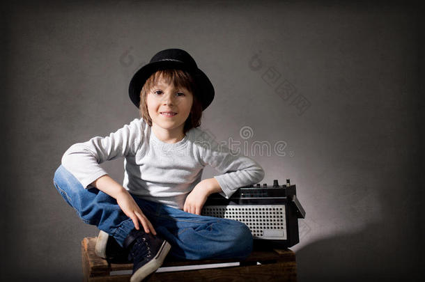 可爱的男孩戴着黑色的帽子，坐在木制托盘上，拿着收音机