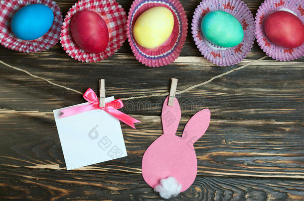 五颜六色的复活节彩蛋和纸兔。 木制背景上的贺卡。 复活节商品库存。