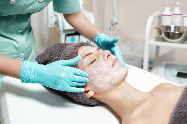 美容师在水疗沙龙里给美丽的年轻女人戴上面膜。 化妆品程序皮肤护理。 微磨擦