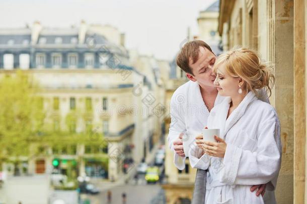 一对穿着白色浴袍的夫妇在阳台上一起喝咖啡