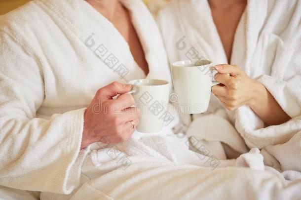 一对穿着白色浴袍的夫妇在床上一起喝咖啡