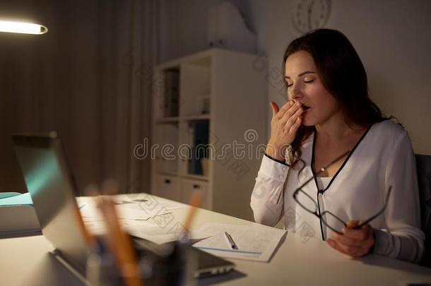 疲倦的女人和文件打呵欠在夜办公室