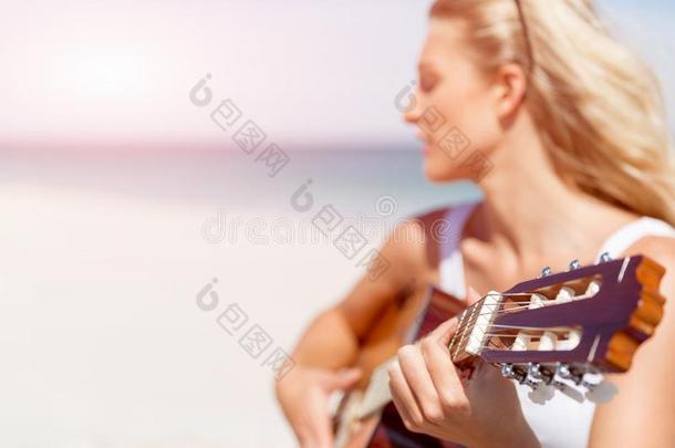 美丽的年幼的女人演奏吉他向海滩