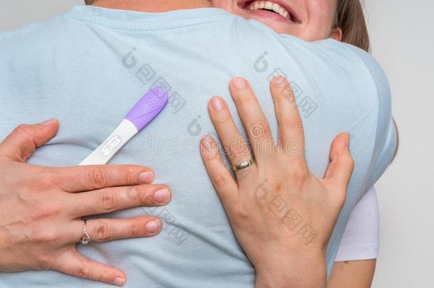 女人和积极的怀孕试验热烈地拥抱她丈夫