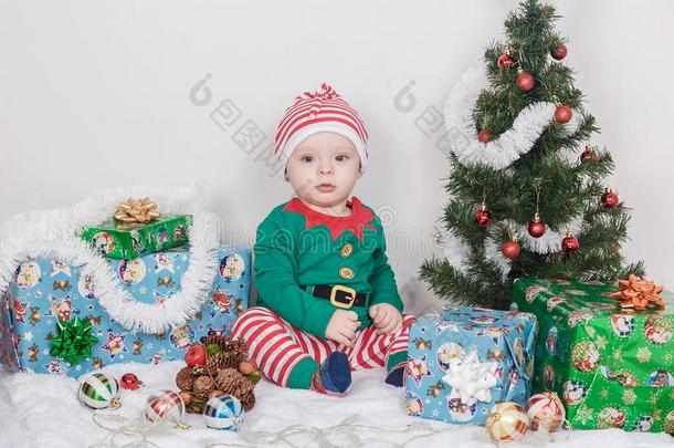 男孩采用圣诞节小精灵戏装.一婴儿在近处一圣诞节树.