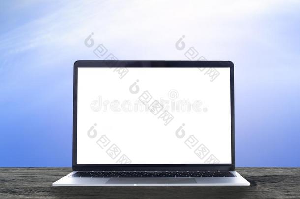 便携式电脑和白色的空白的屏幕向木制的表和蓝色天背