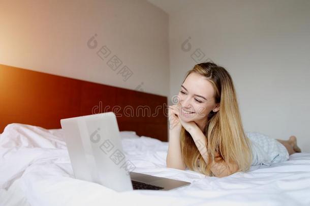 年幼的女人有样子的在便携式电脑工作的家遥远地在白色的床