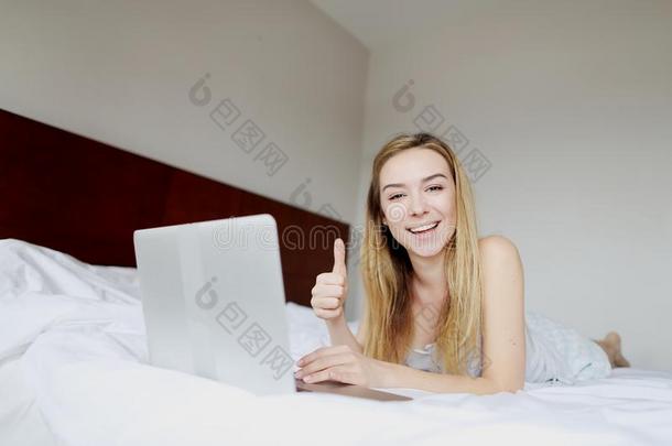 年幼的女人幸福的给看喜欢拇指在上面和便携式电脑工作的家英语字母表的第18个字母