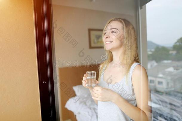 漂亮的年幼的女人和水看在阳台后的醒在上面和