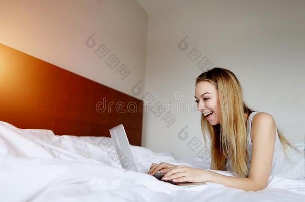 女人超级的幸福的和便携式电脑工作的家遥远地在白色的床