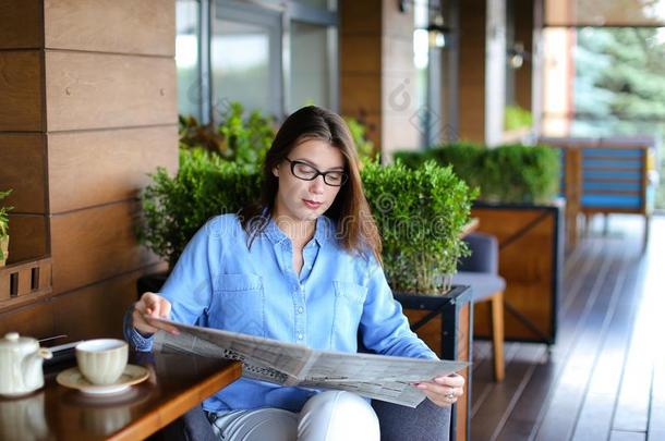 年幼的女人阅读报纸和使用智能手机在饭店