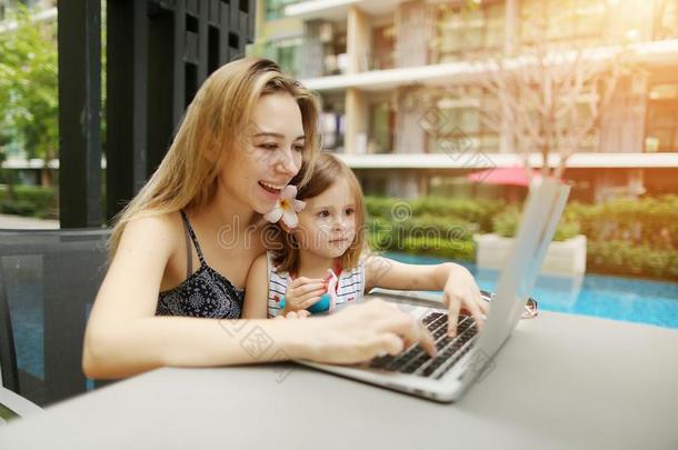 母亲和女儿使用便携式电脑向背景关于游泳水池向