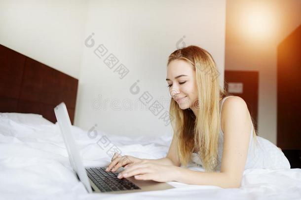 年幼的女人幸福的和便携式电脑工作的家遥远地在白色的床