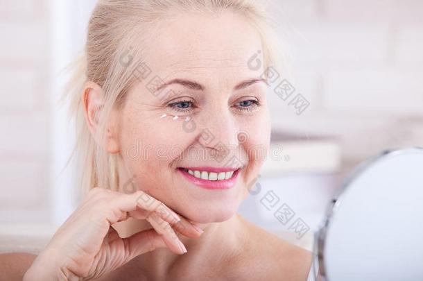 四十<strong>年</strong>老的女人有样子的在皱纹采用镜子.塑料制品在来自古法语的英语中与super-同义