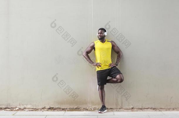 像运动家的非洲式发型男人起立在近处老的墙,做早晨体操