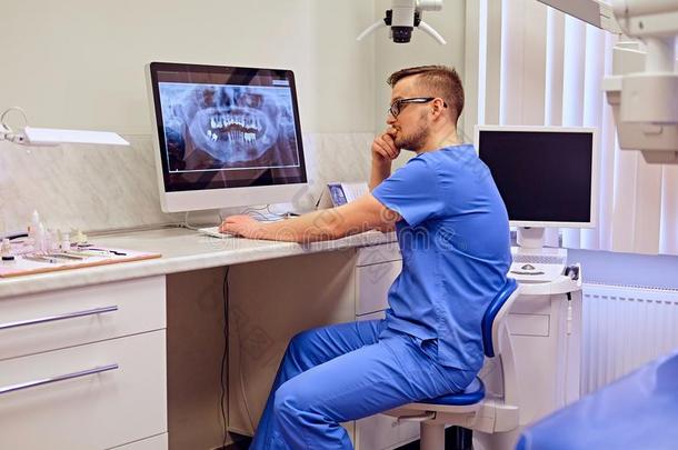 牙科医生有样子的在牙字母x-射线向指已提到的人计算机采用一牙科医生奥菲