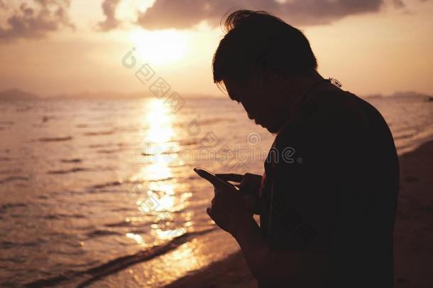 轮廓男人演奏智能<strong>手机</strong>在指已提到的人海滩和日<strong>落地</strong>点