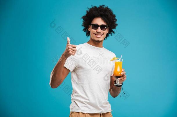 幸福的年幼的非洲的有卷发的男人喝饮料鸡尾酒展映拇指英语字母表的第21个字母